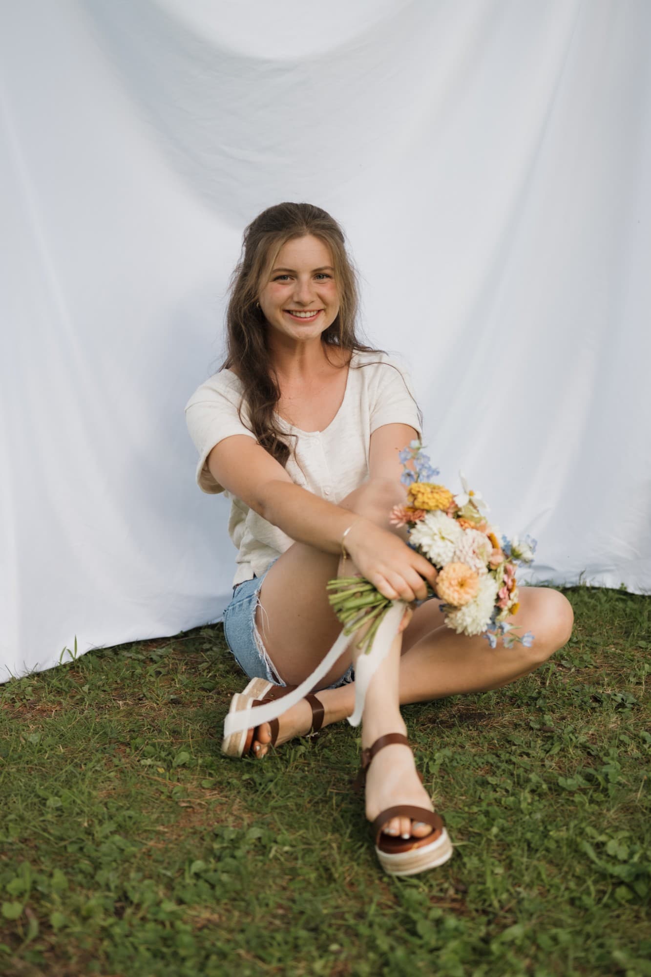 Emma of Wildflower Gardens sitting on the grass holding a fresh-cut bouquet